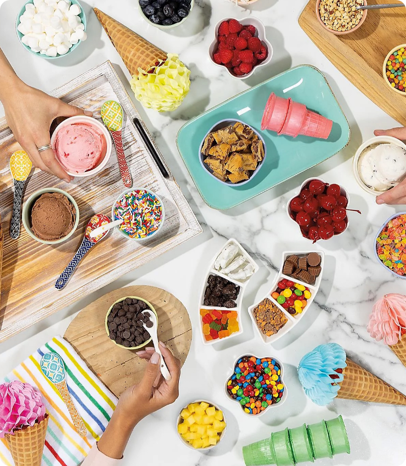 Επιλογές topping για παγωτό από ψηλά: φρούτα, σοκολατάκια, γκοφρέτες, ζαχαράκια και κώνοι παγωτού σε μαρμάρινη επιφάνεια