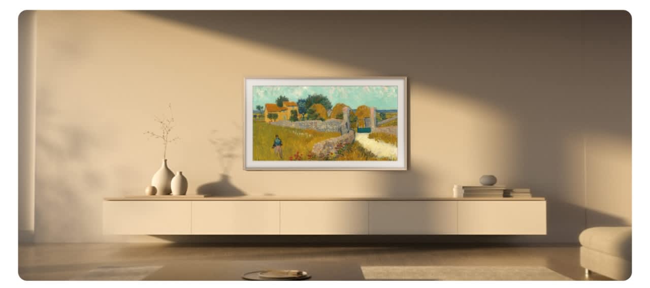 Η Samsung The Frame κρεμασμένη στον τοίχο σαν πίνακας ζωγραφικής, χωρίς ορατά καλώδια, πάνω από ξύλινο έπιπλο σε φωτεινό σαλόνι