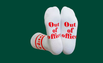 Λευκές κάλτσες με την επιγραφή 'Out of Office' σε κόκκινο, χιουμοριστικό δώρο Secret Santa.